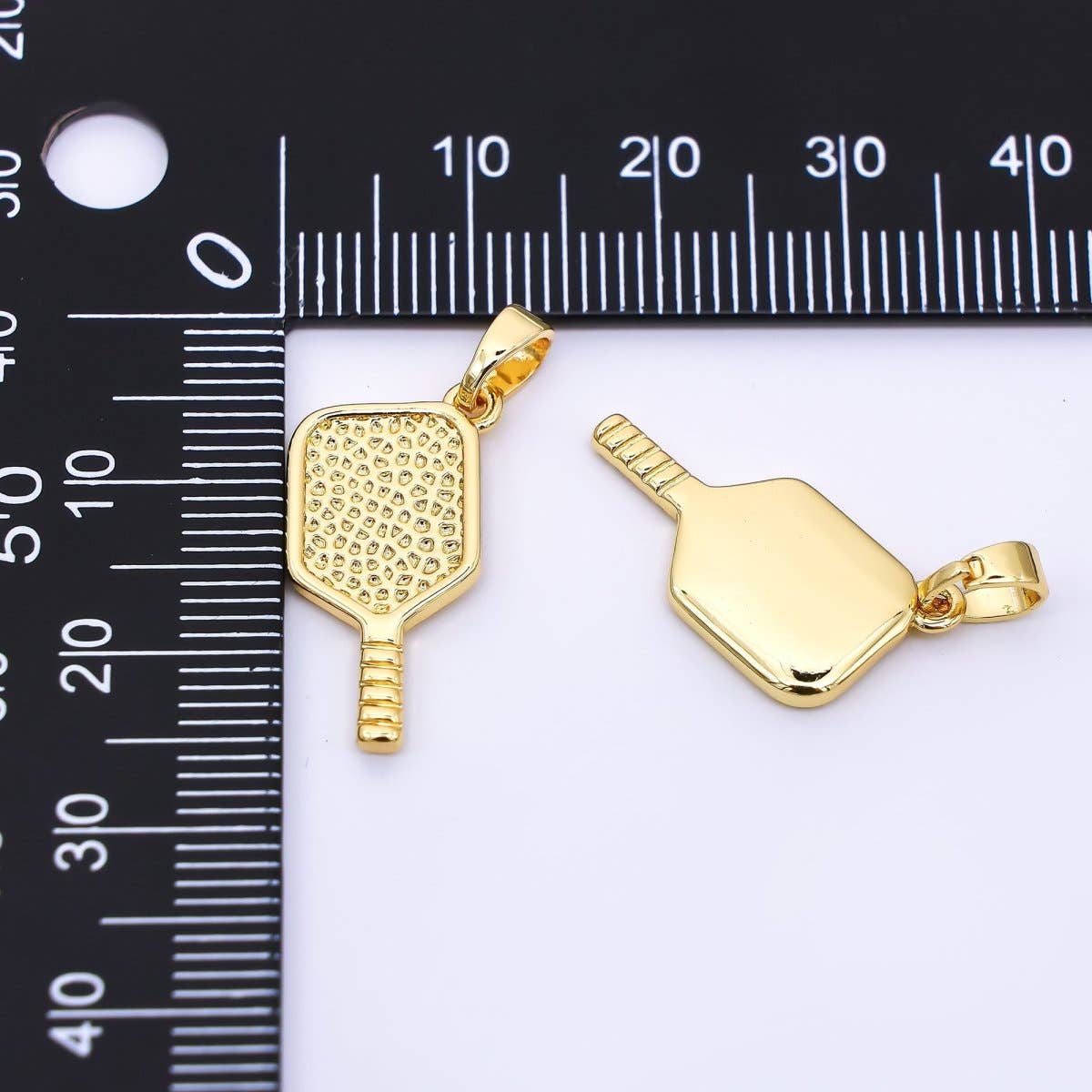 Two gold pickleball paddle pendants on a white background with a ruler for scale.