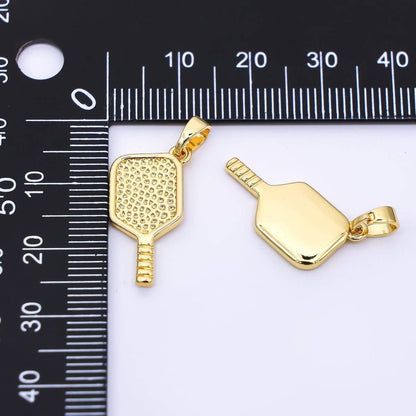 Two gold pickleball paddle pendants on a white background with a ruler for scale.