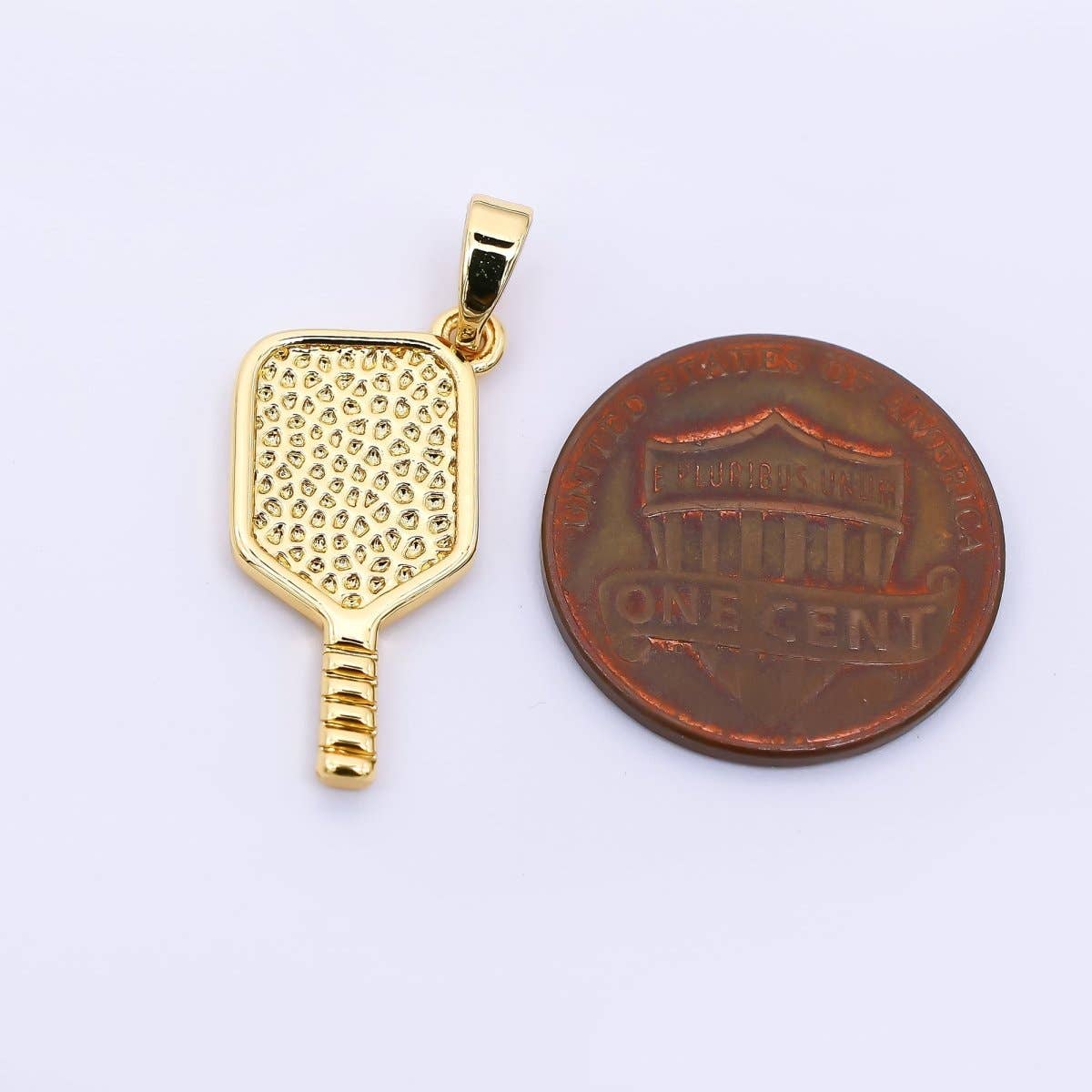 Gold pickleball paddle pendant next to a penny on a white background