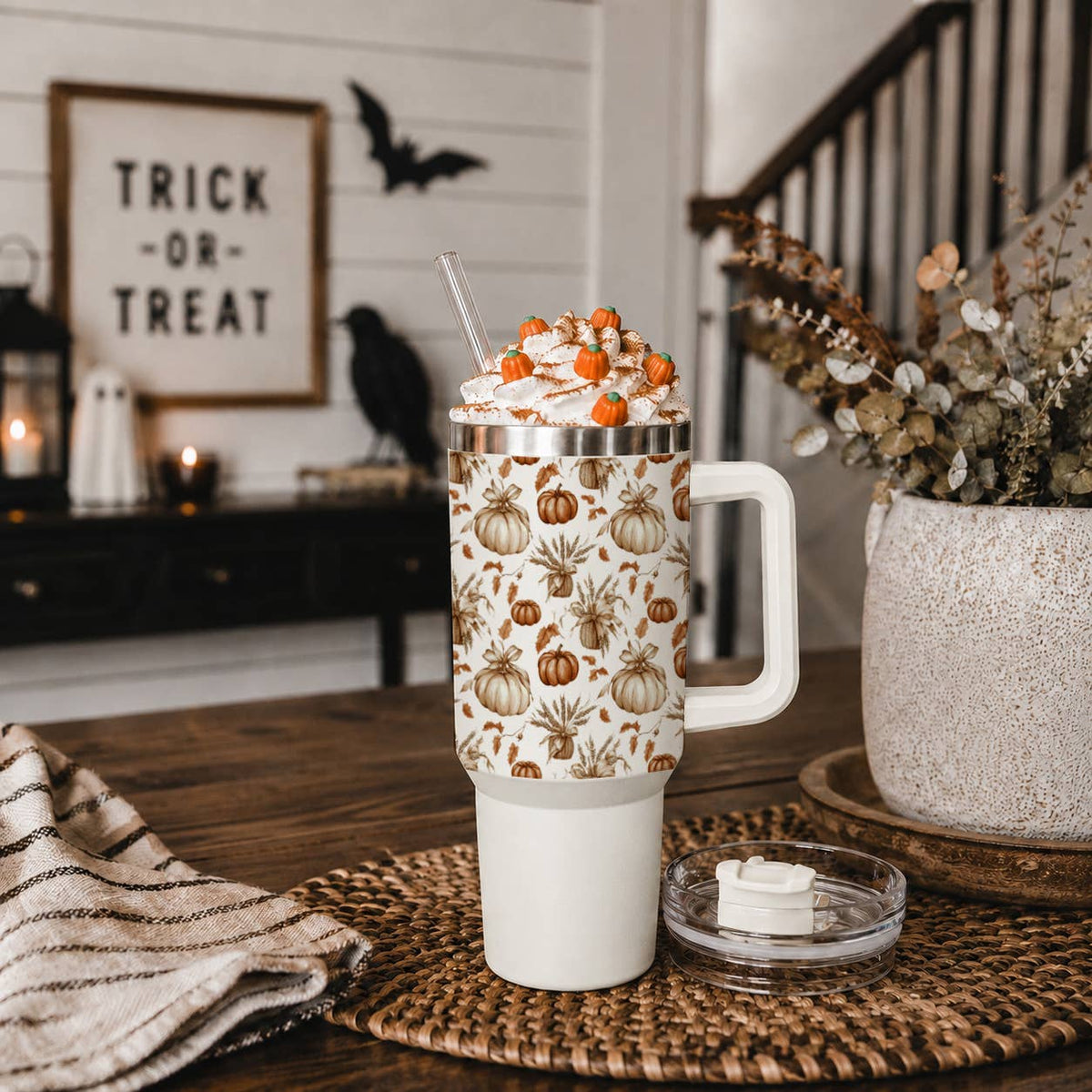 White tumbler with pumpkin pattern on a wooden table with Halloween decorations in the background.
