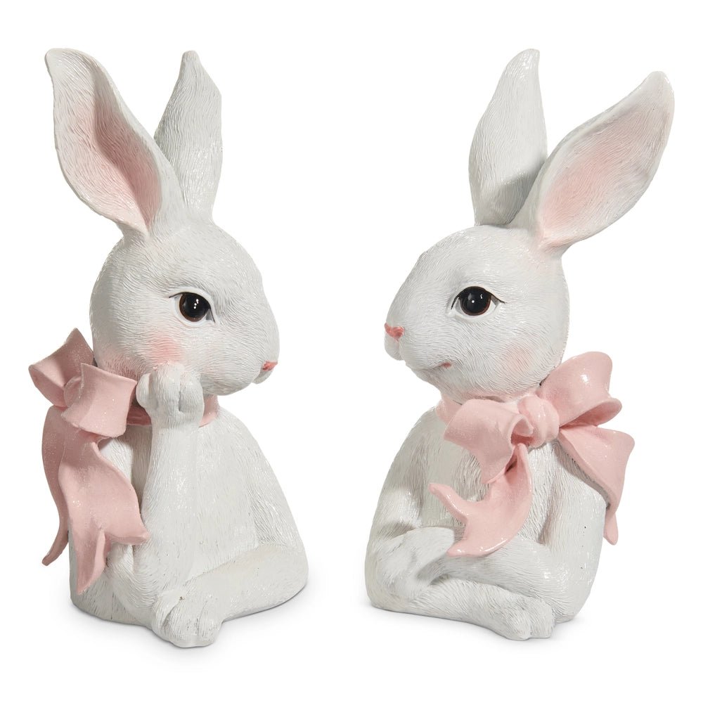 Two white rabbit figurines with pink bows on a white background