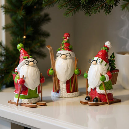 Three decorative Santa Claus figurines on a surface with a blurred Christmas tree in the background.