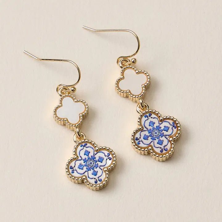 Pair of gold earrings with blue floral designs on a beige background
