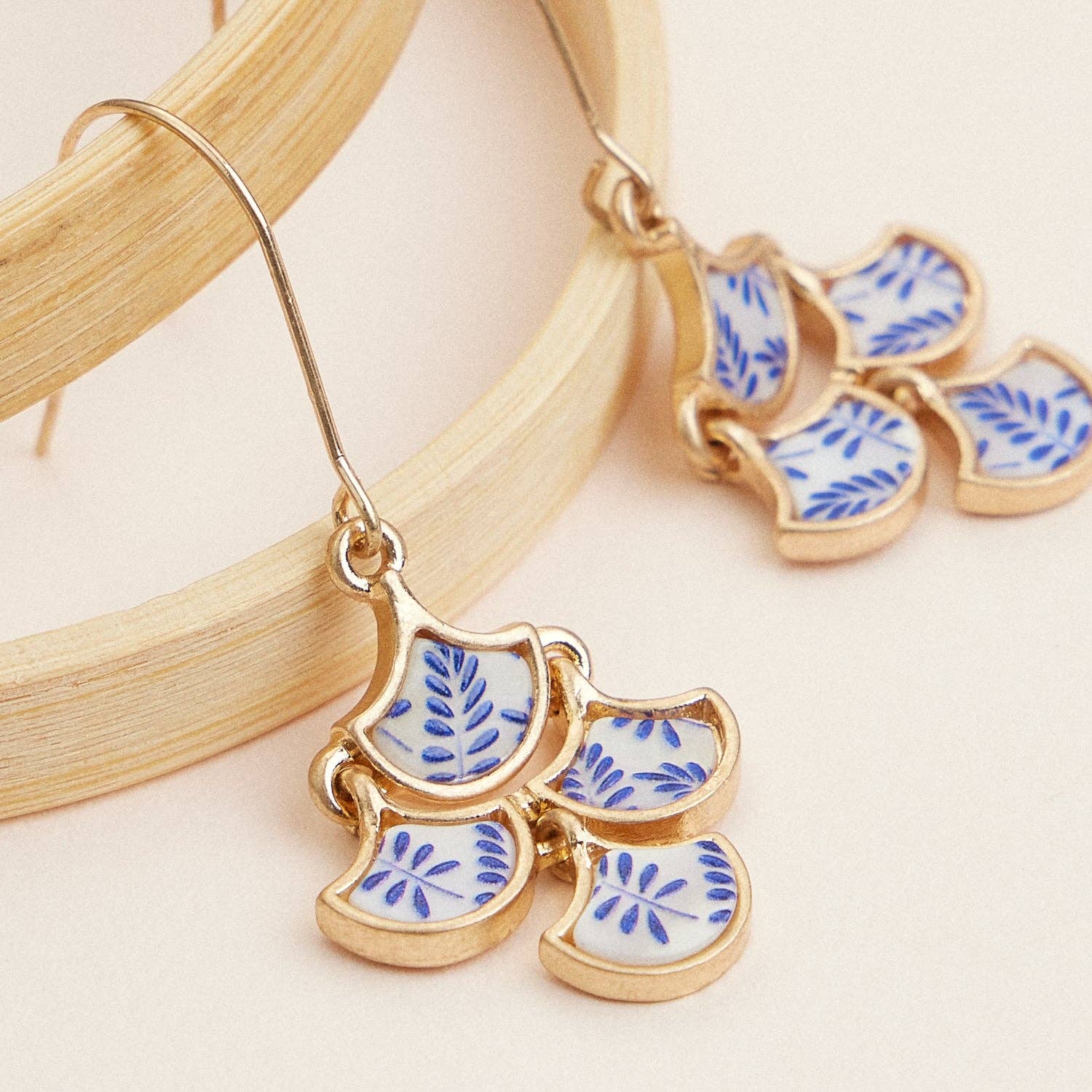 Gold earrings with blue and white floral designs on a beige background