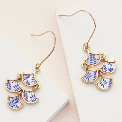Gold earrings with blue leaf patterns on a white surface