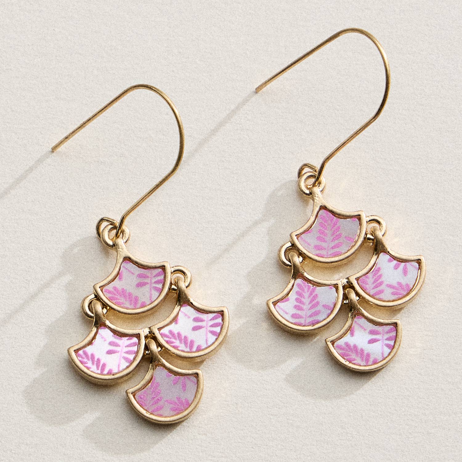 Pair of gold earrings with pink leaf patterns on a light background