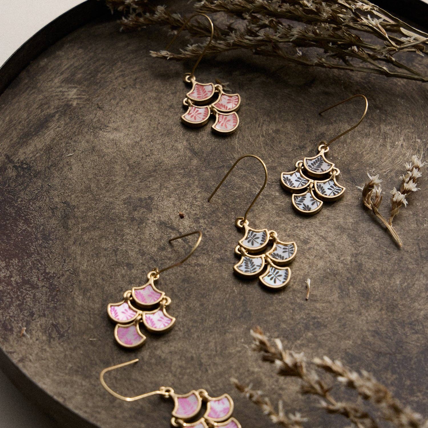 Gold and pink earrings on a textured surface with dried plants.