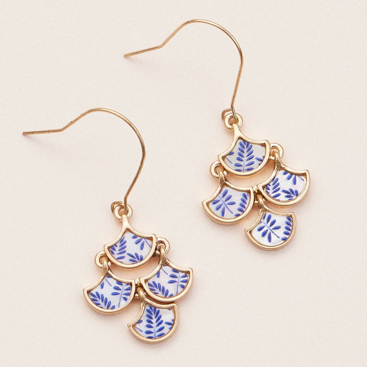 Gold earrings with blue and white pattern on a beige background
