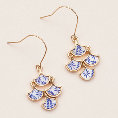 Gold earrings with blue and white pattern on a beige background