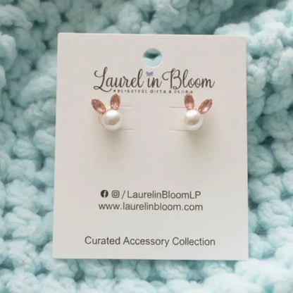 Pair of pearl earrings on a 'Laurel in Bloom' branded card against a textured blue background.