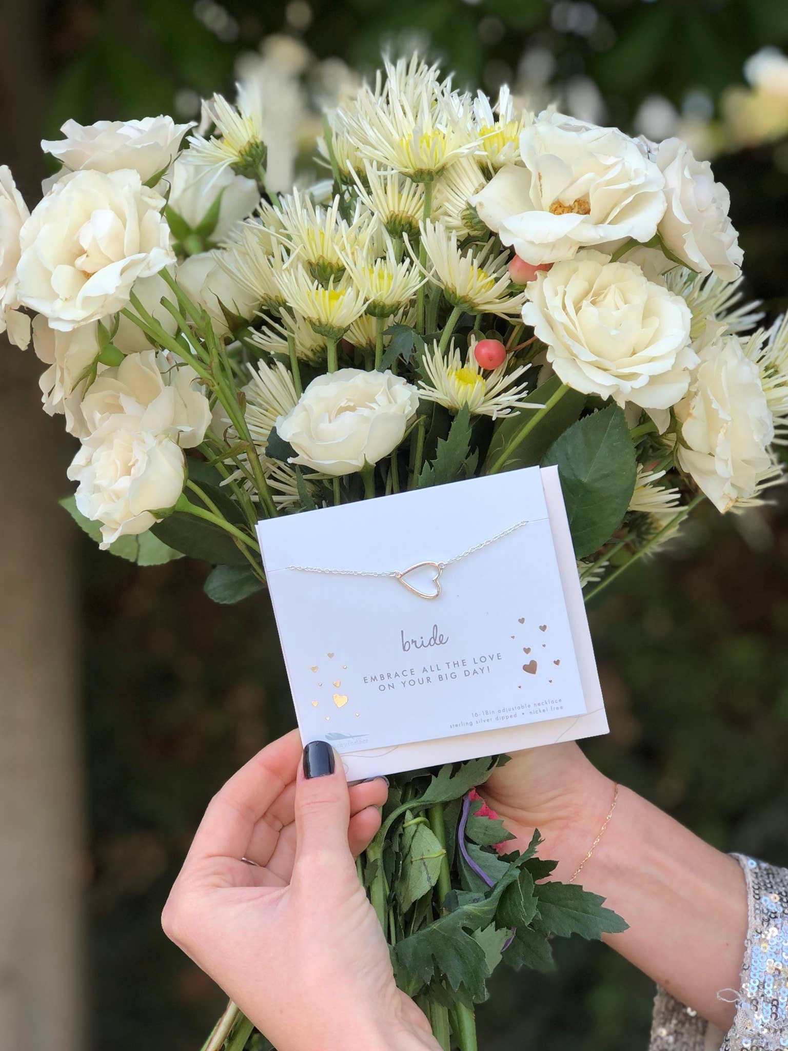 Bouquet of white flowers held by a person with a necklace card in the center.
