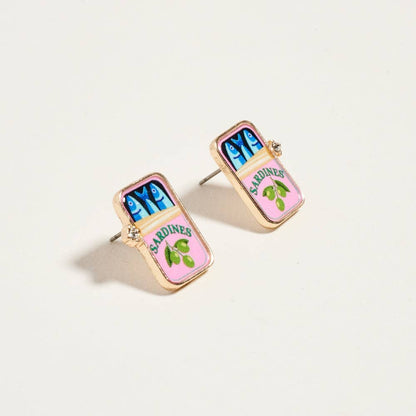 Earrings resembling sardine can packaging on a light beige background