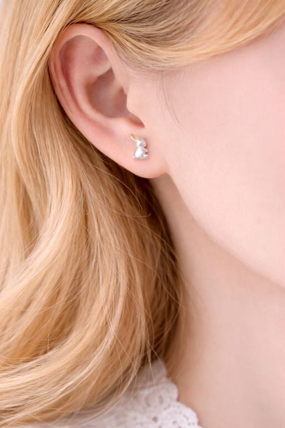 Close-up of an ear wearing a small earring with blonde hair.
