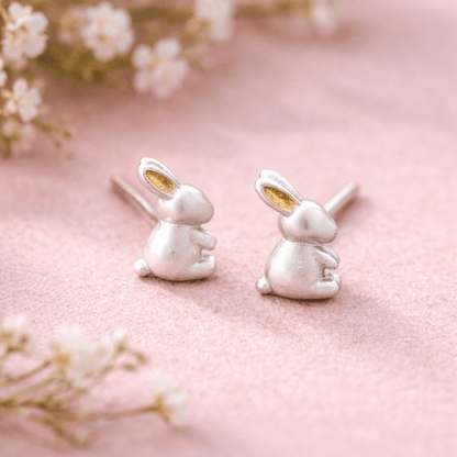 Silver rabbit-shaped earrings on a pink background with floral elements.