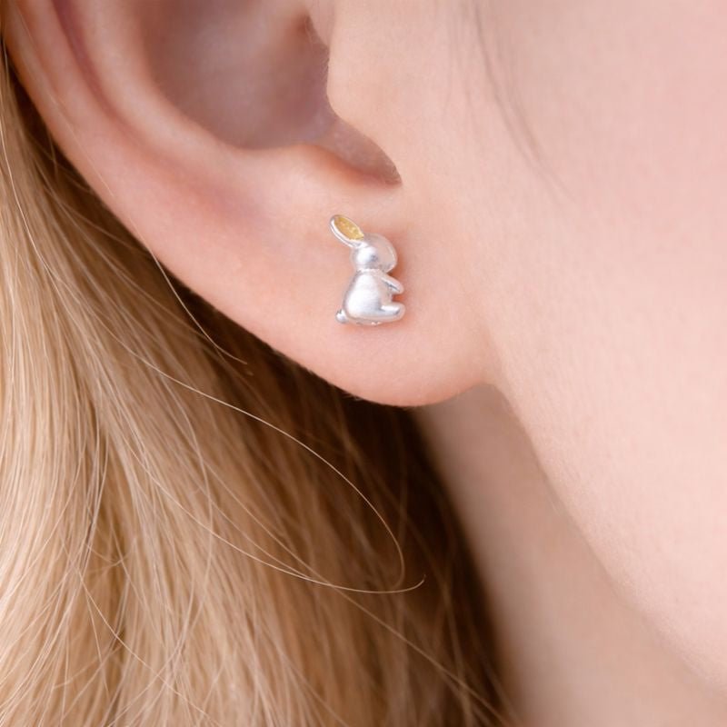 Silver bunny-shaped earring worn by a person with blonde hair.