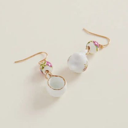Pair of earrings with white beads and floral designs on a beige background