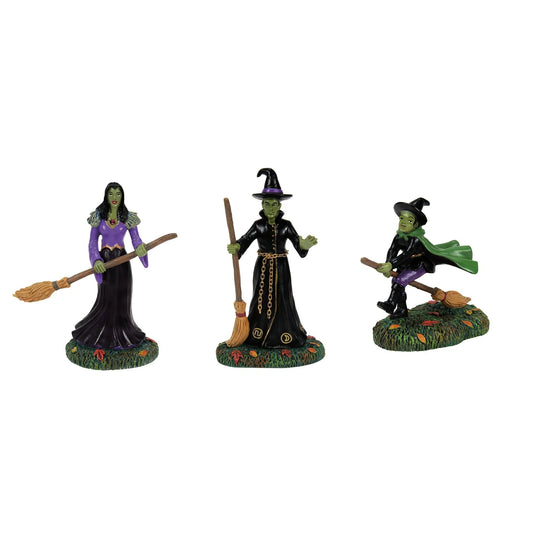Three witch figurines with brooms on a white background