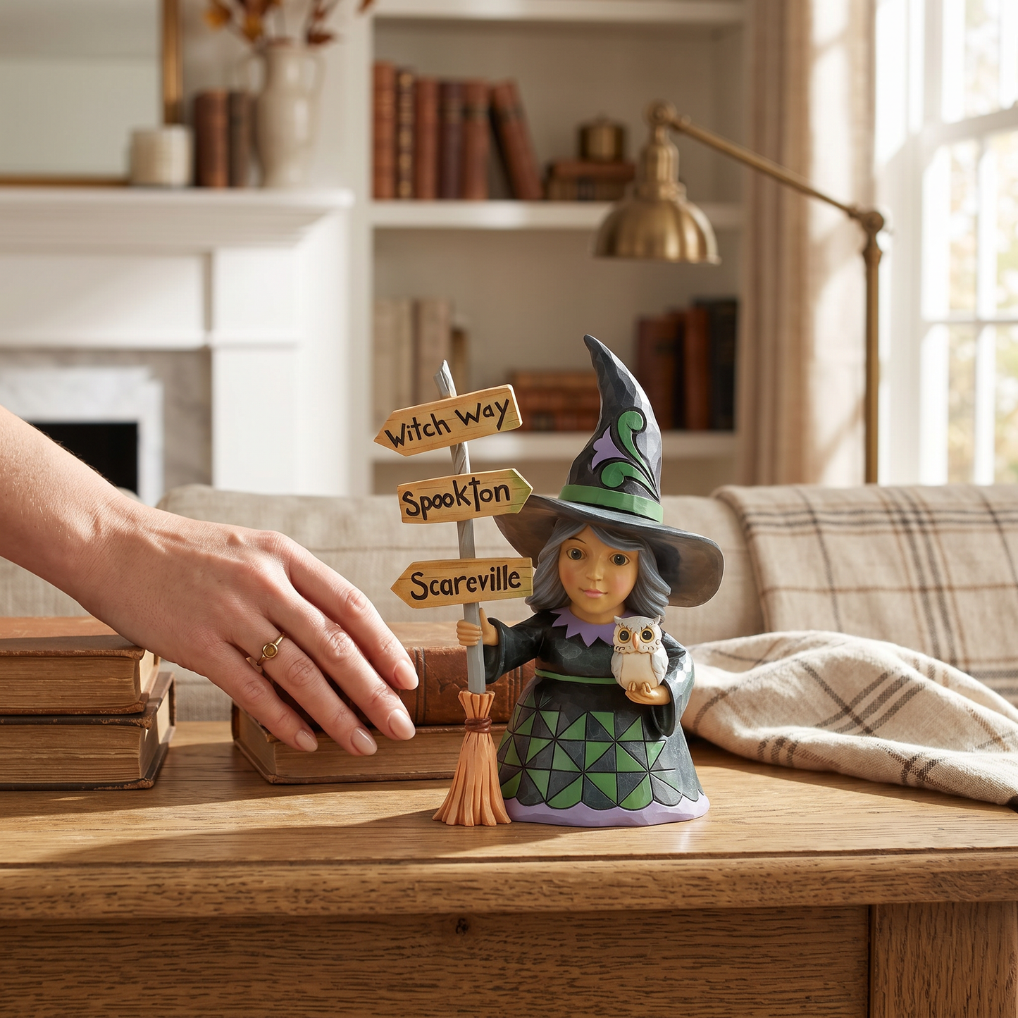 Halloween-themed figurine with a witch and owl on a wooden table, surrounded by books and decor.