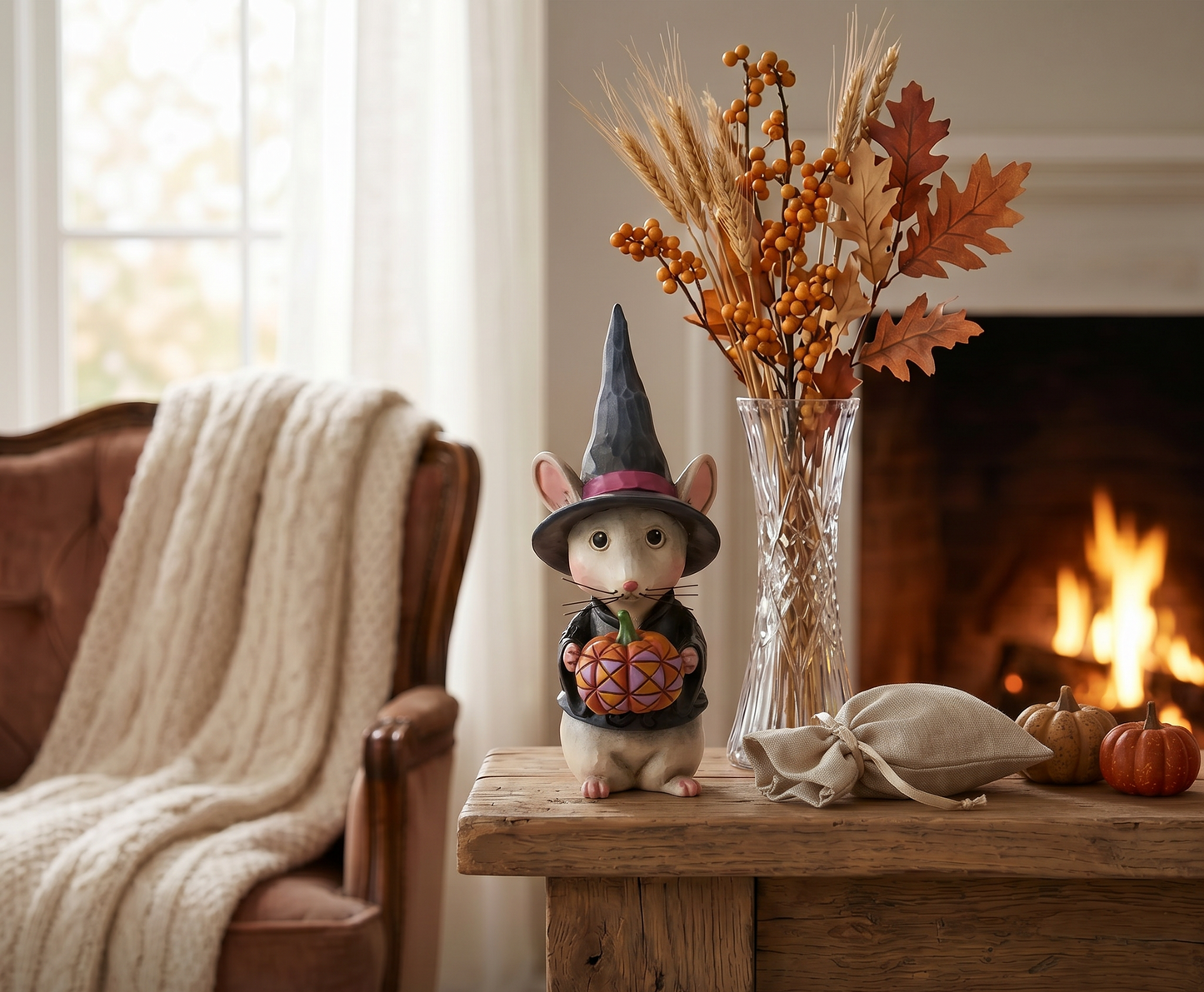 Decorative mouse in a witch hat with pumpkins on a wooden table in front of a fireplace.