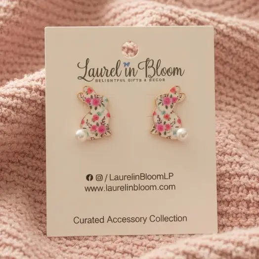 Floral cat-shaped earrings on a 'Laurel in Bloom' card against a pink textured background
