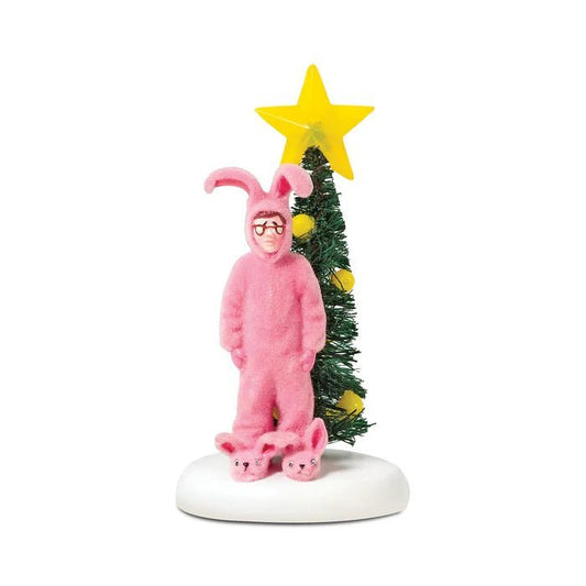 Person in a pink bunny suit standing next to a small decorated Christmas tree with a yellow star on a white background.