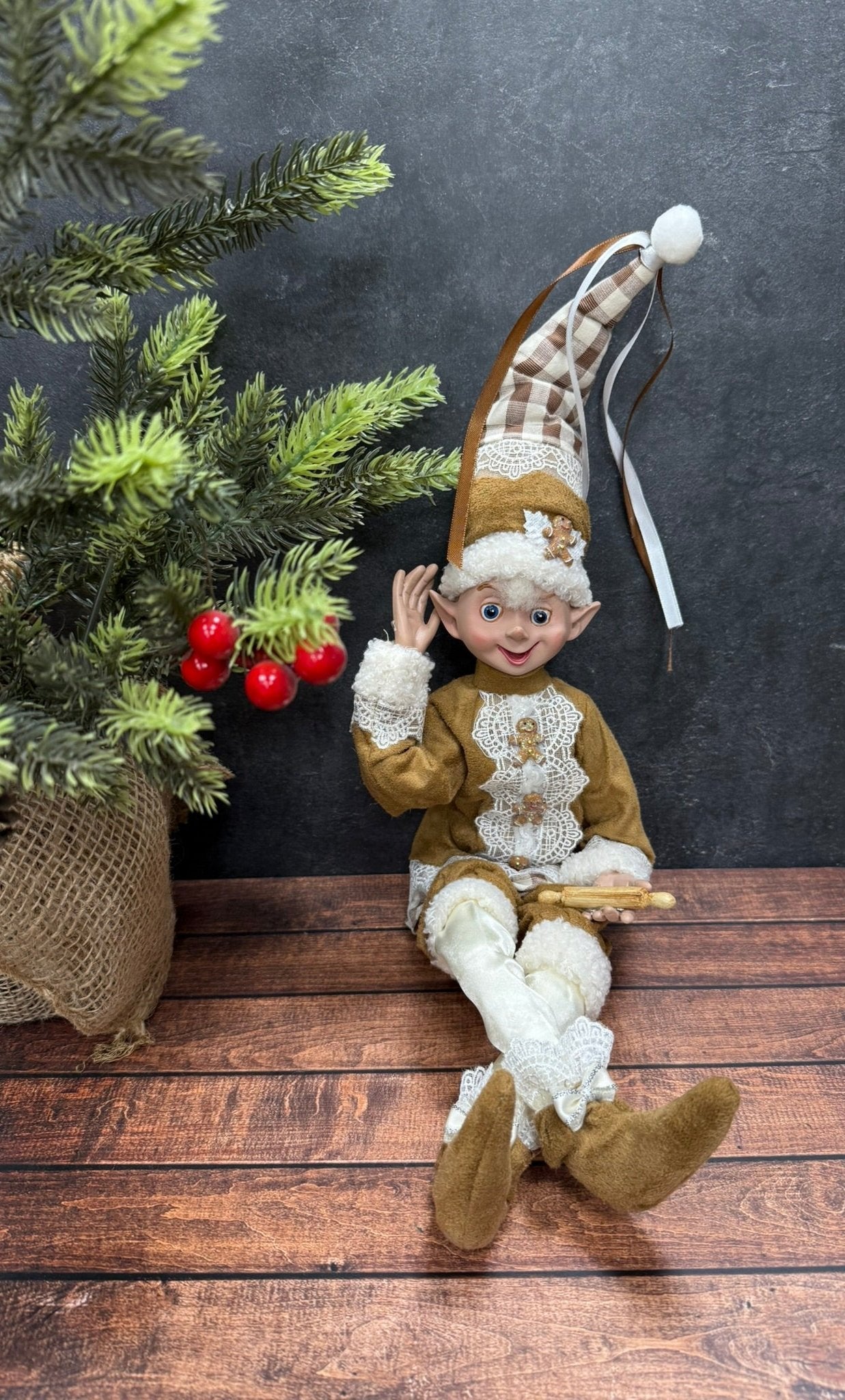 Elf figurine sitting on a wooden surface with a dark background and Christmas decorations.
