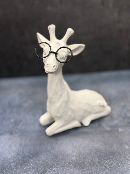 White giraffe figurine wearing black glasses on a gray surface with a dark background