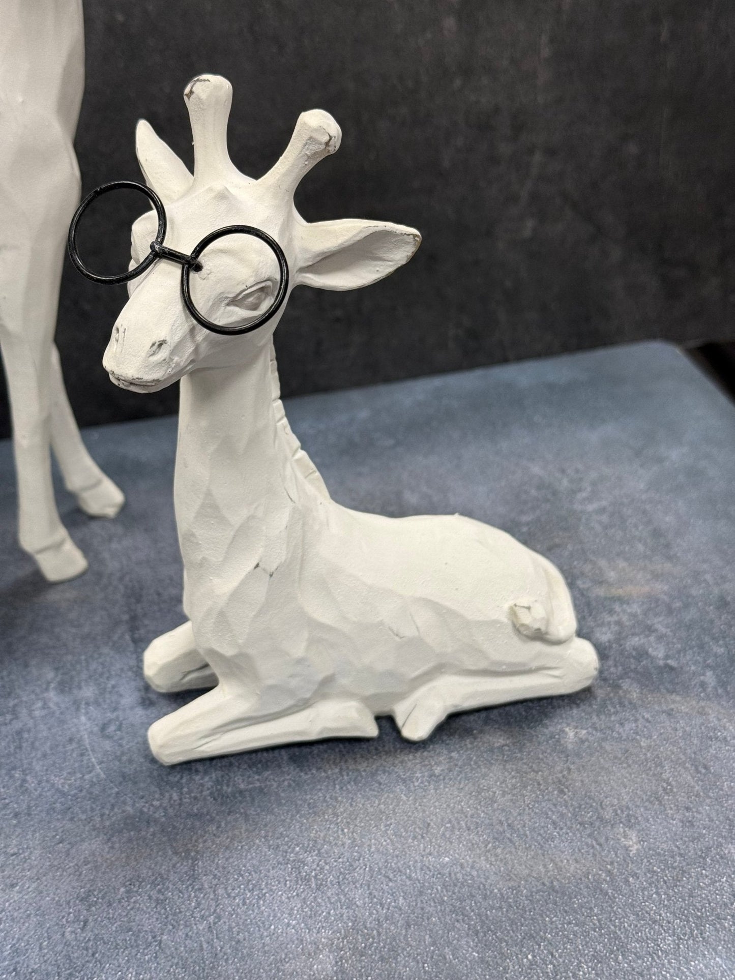 White Giraffe figurine wearing black glasses on a gray surface