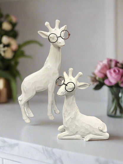 Two white Giraffe figurines wearing glasses on a surface with flowers in the background.