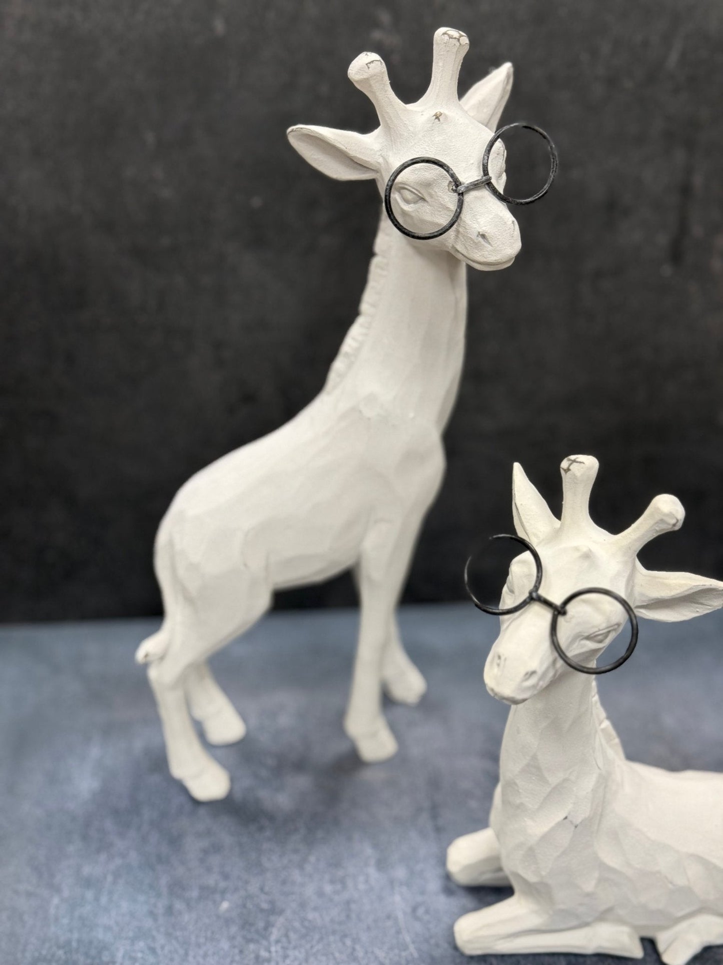 Two white ceramic giraffe figurines wearing round glasses on a dark background.