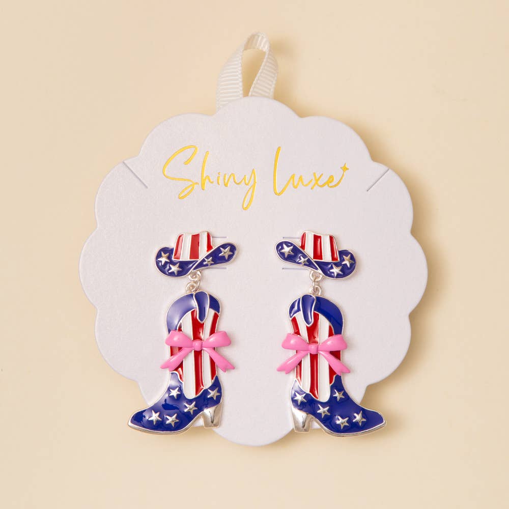 Pair of earrings shaped like cowboy boots with American flag design on a 'Shiny Luxe' branded card.