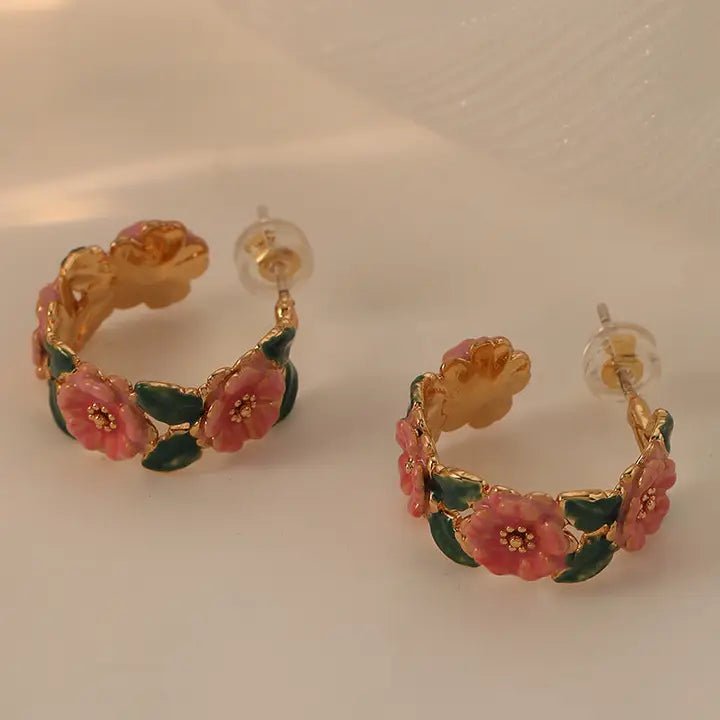 Gold hoop earrings with pink floral designs on a light background
