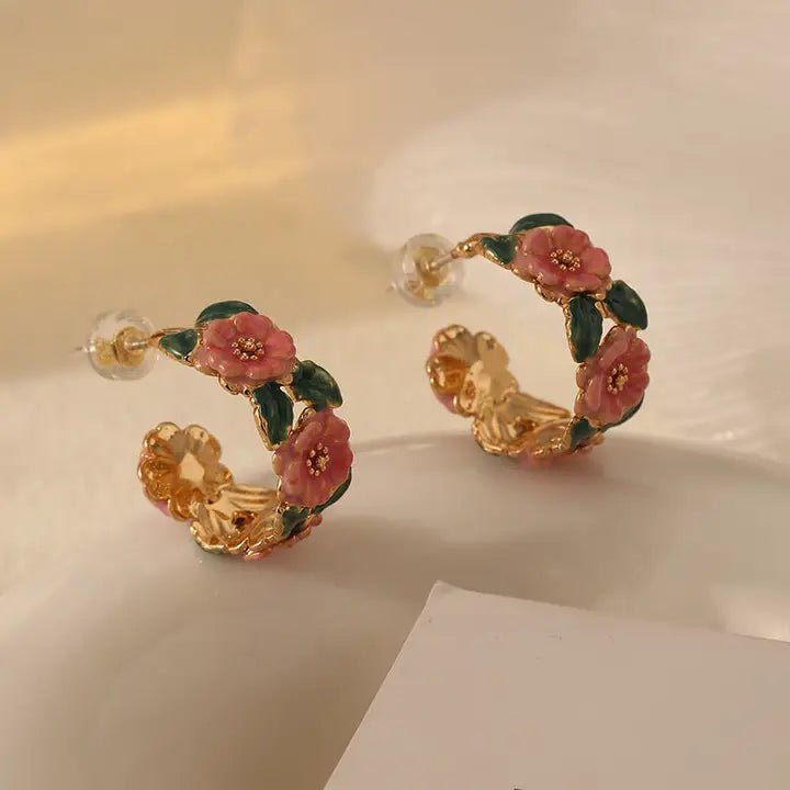 Gold hoop earrings with pink floral designs on a beige background