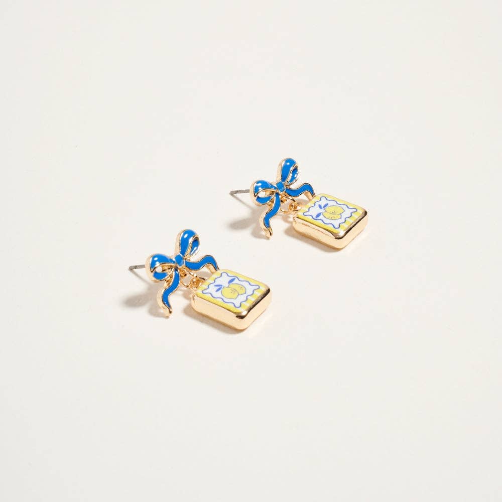 Pair of earrings with blue bows and yellow floral designs on a light beige background