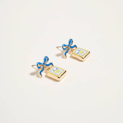 Pair of earrings with blue bows and yellow floral designs on a light beige background