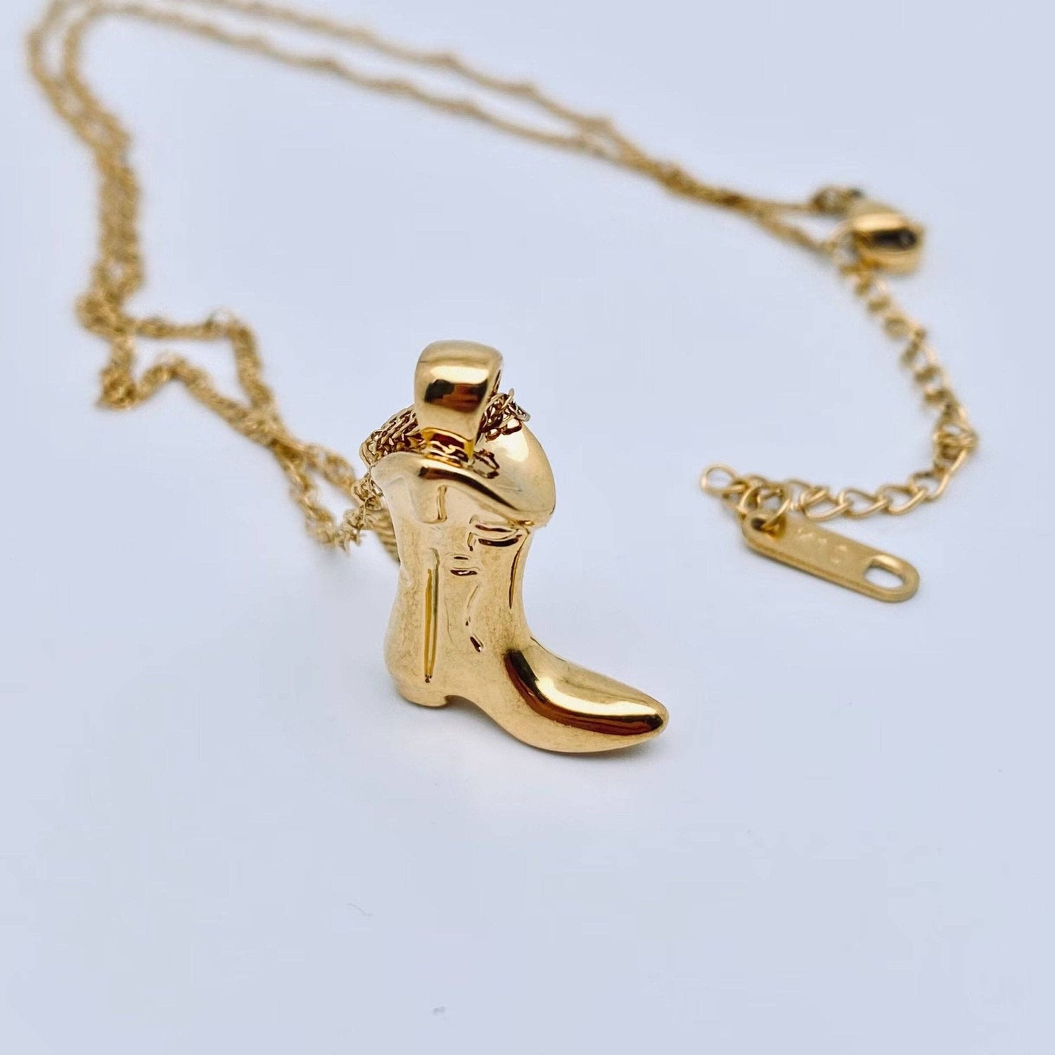 Gold cowboy boot pendant on a chain against a light gray background