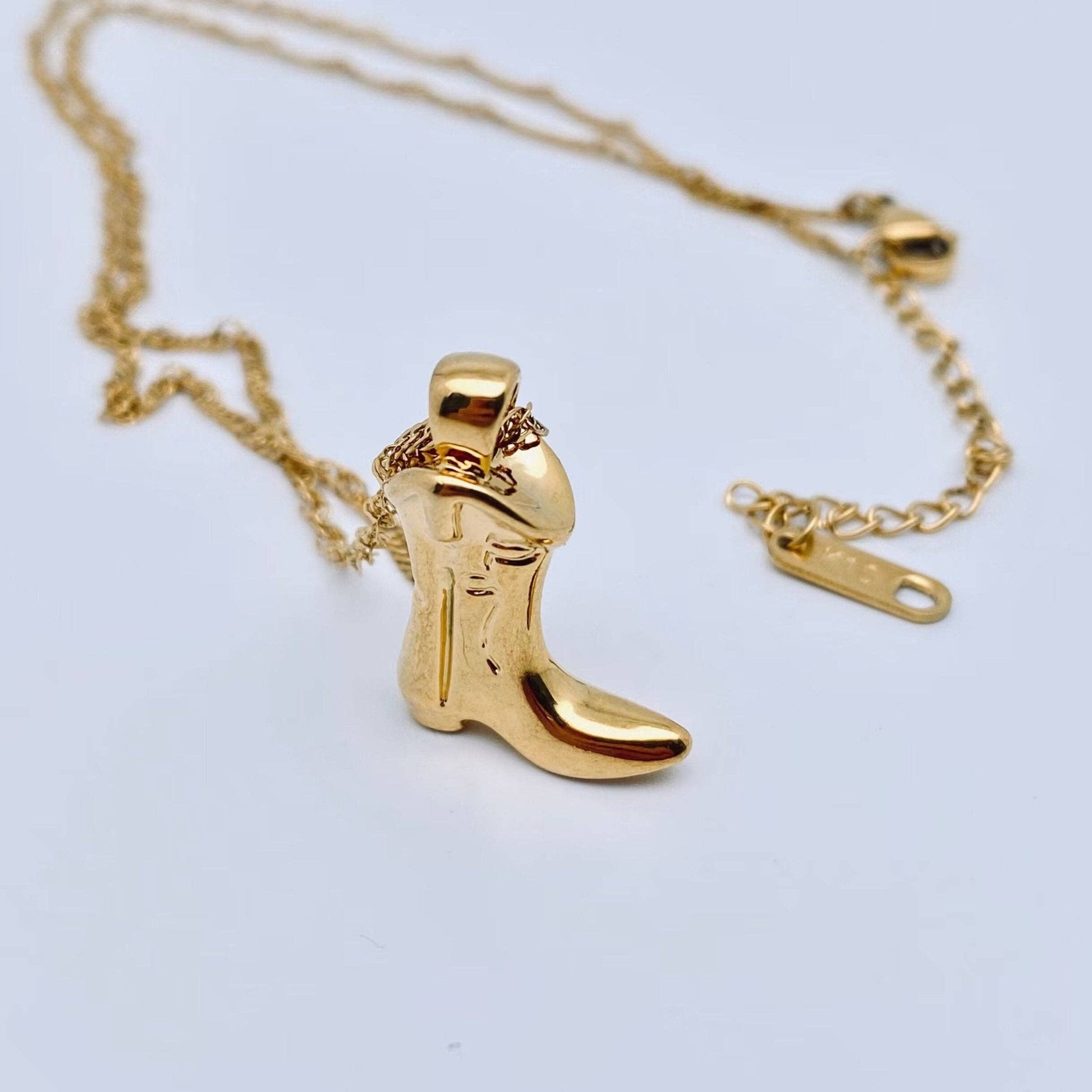 Gold cowboy boot pendant on a chain against a light gray background