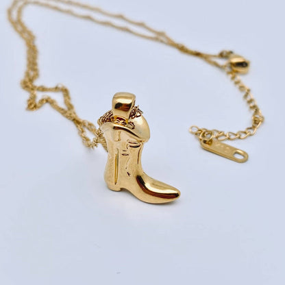 Gold cowboy boot pendant on a chain against a light gray background